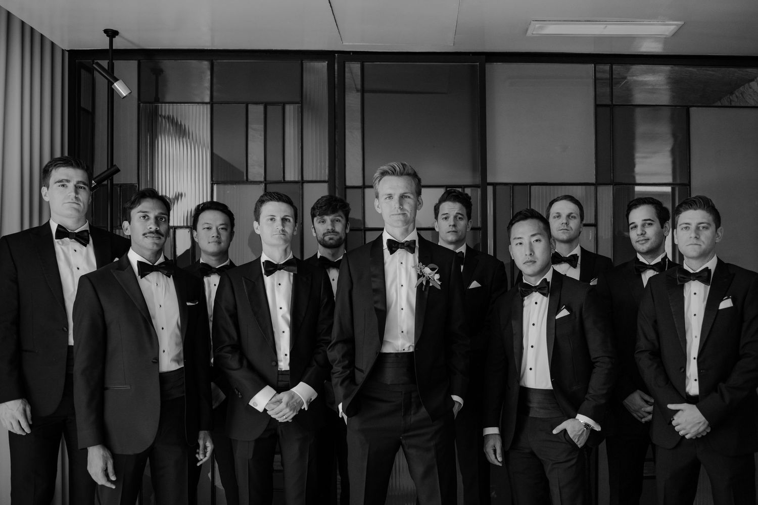 Group of groomsmen in black tuxedos posing together in a stylish black and white wedding photo.