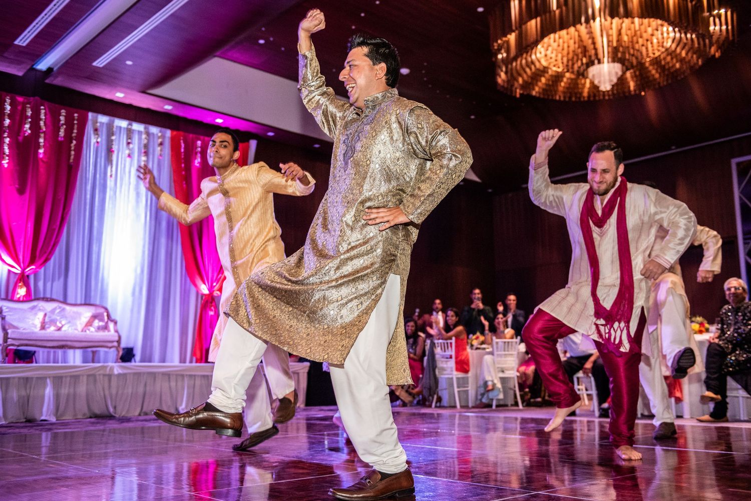 Men and women in traditional Indian attire perform Bollywood dance at a vibrant wedding reception.