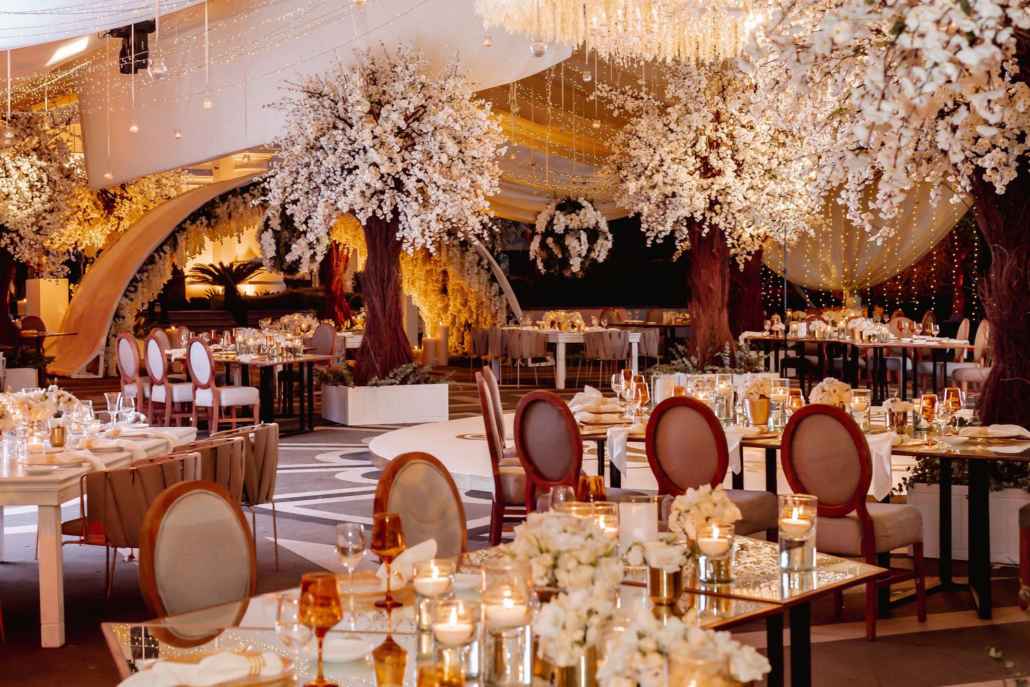 Elegant white wedding reception with crystal chandeliers and sophisticated table settings in warm lighting.