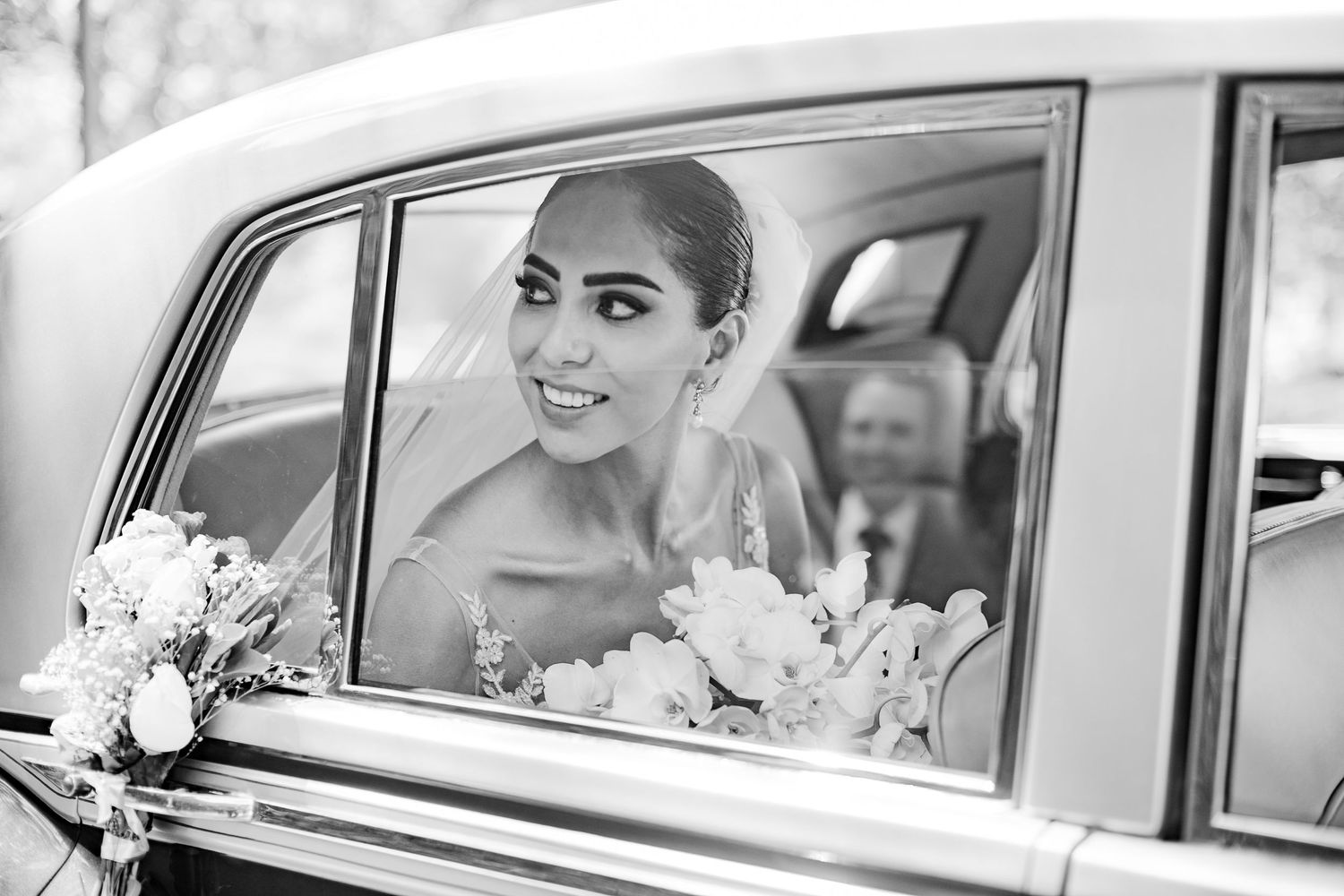 Classic vintage car carries wedding party in elegant black and white photography.