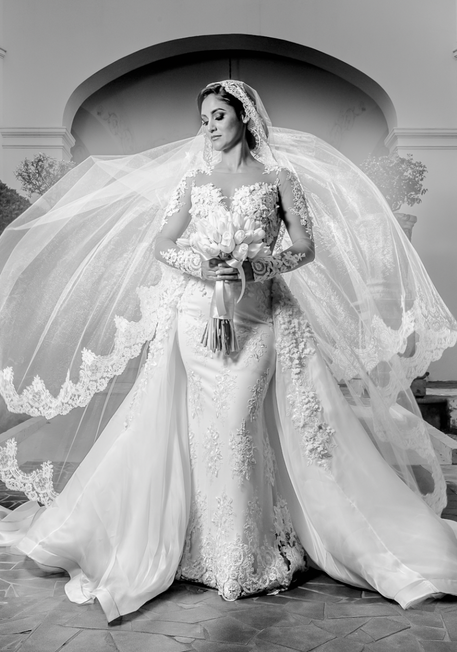 Dramatic bridal portrait featuring lace gown with cathedral veil and train under arched doorway.