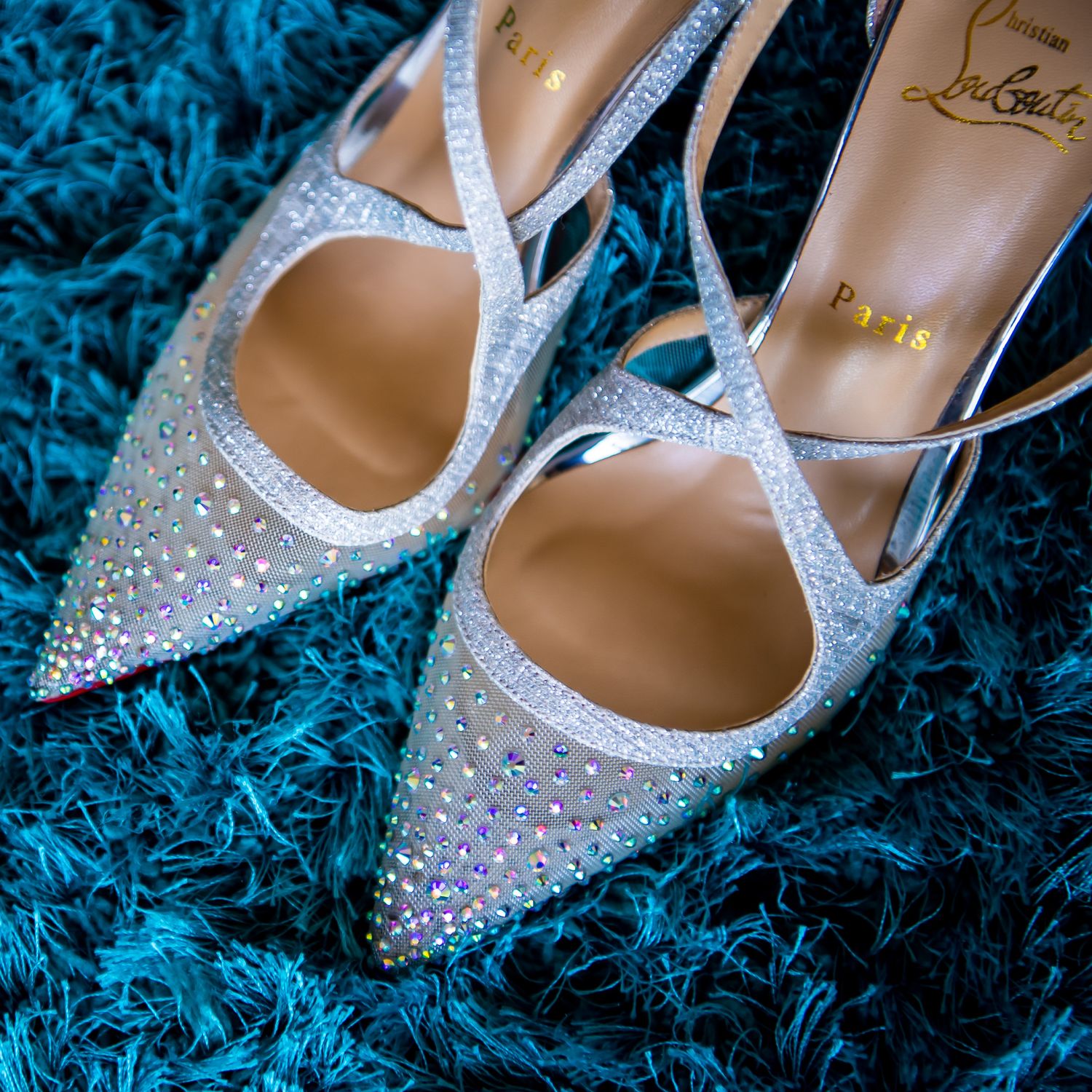 Crystal-embellished bridal shoes with ankle straps on blue textured background.