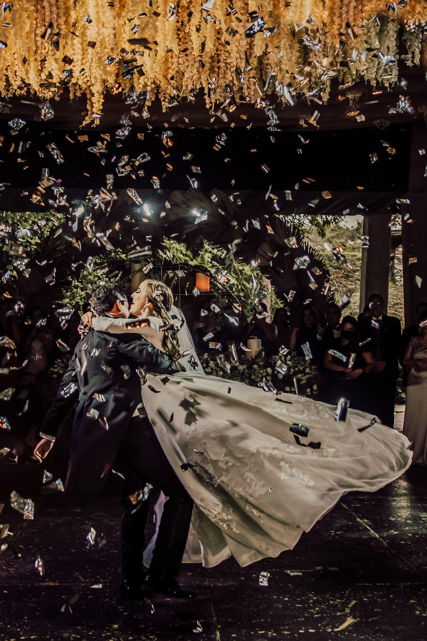 Wedding celebration under hanging floral arrangements with dramatic lighting and floating petals.
