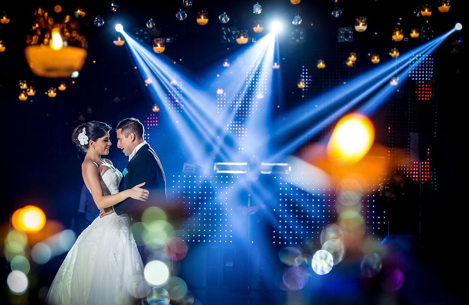 Wedding dance floor illuminated by dramatic blue spotlights and twinkling decorative lights.