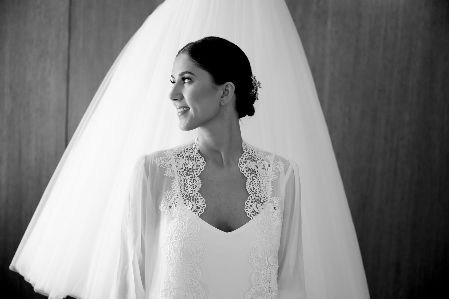Black and white photo of a bride in lace wedding gown and veil, smiling softly in elegant bridal portrait.
