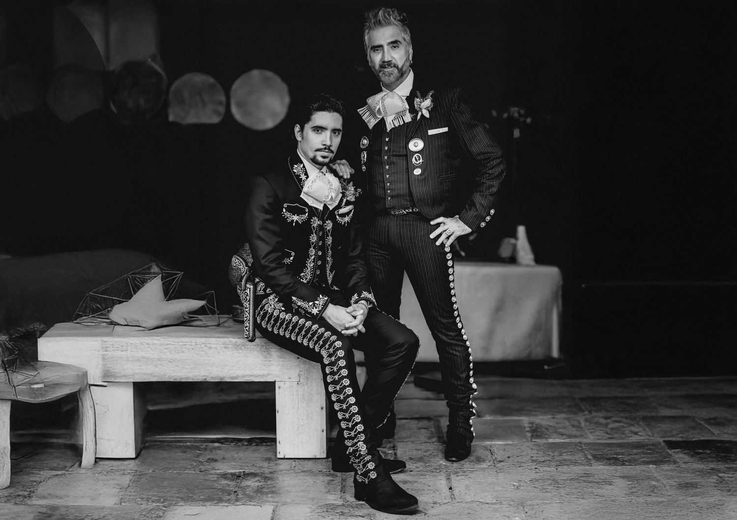 Two men in elegant mariachi suits pose together in a black and white photo at a formal event.