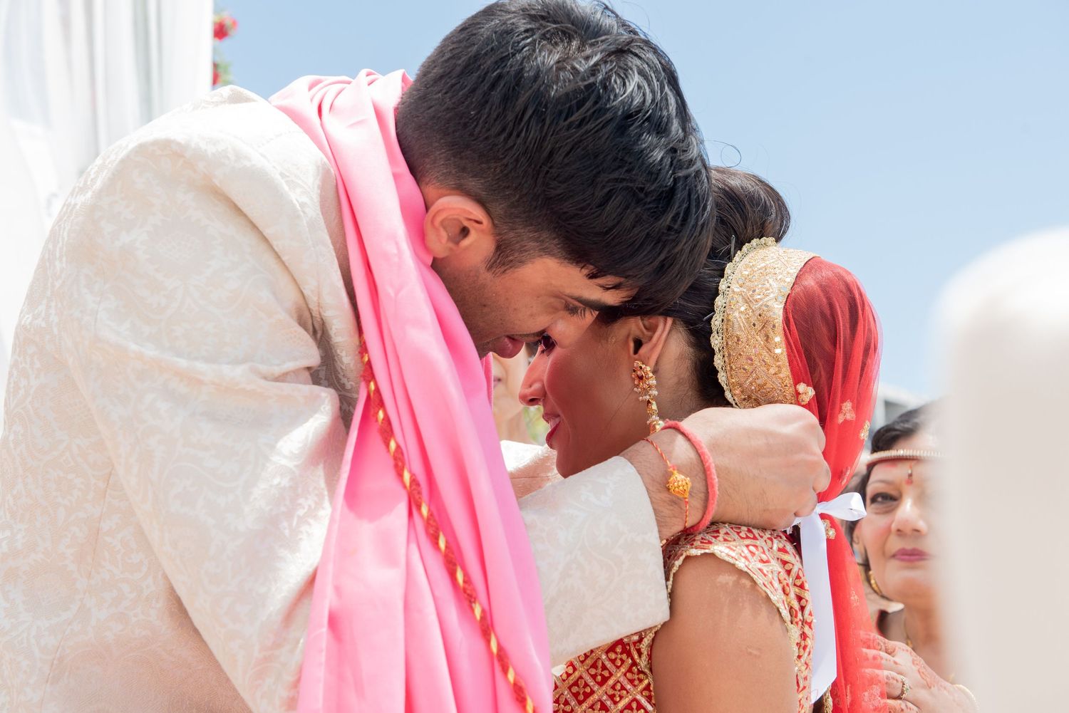 Groom in white sherwani shares intimate moment with bride in pink and gold attire at Indian wedding ceremony.