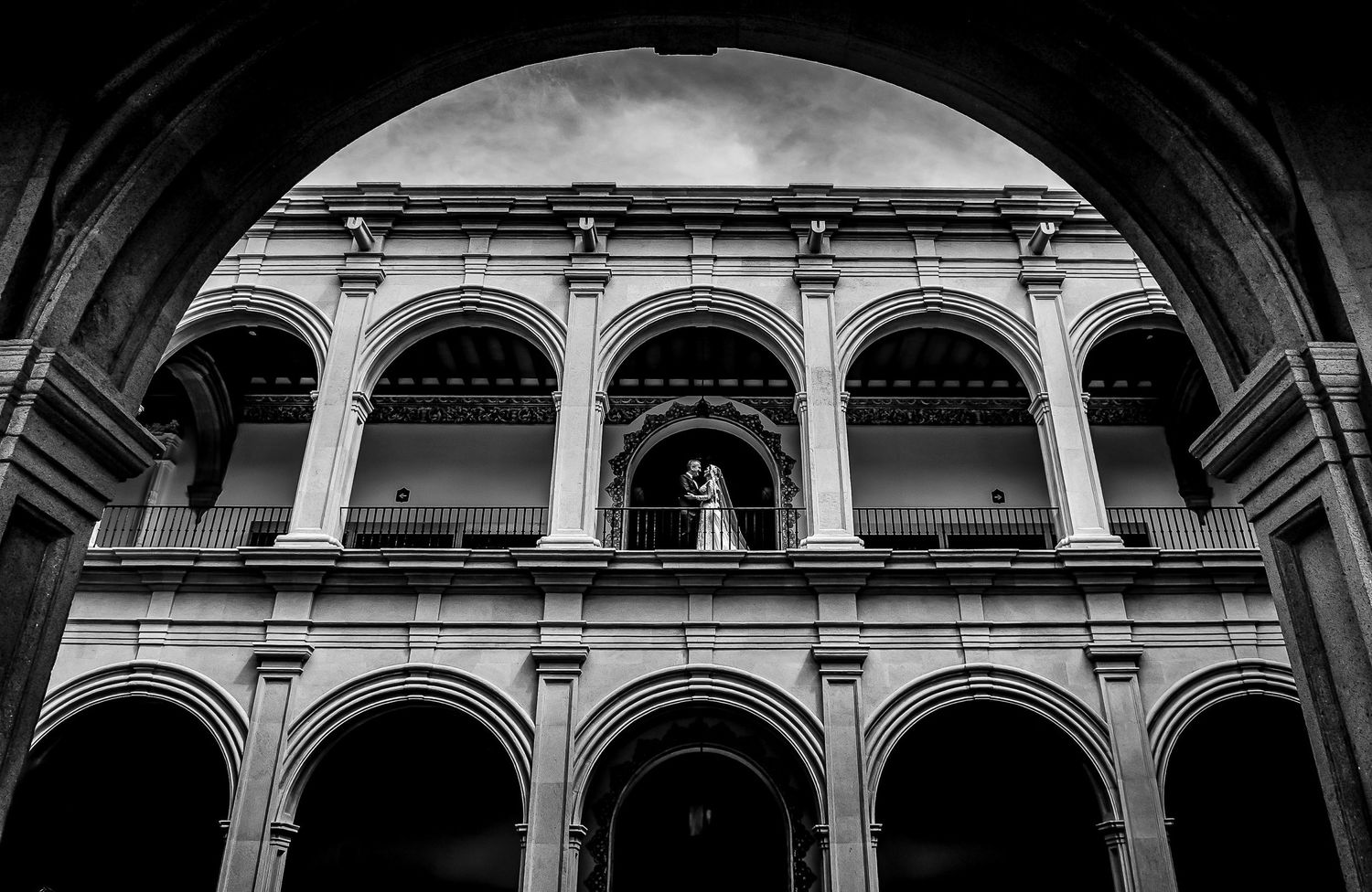 Black and white photo of ornate arched colonnade facade viewed through grand archway of historic building.