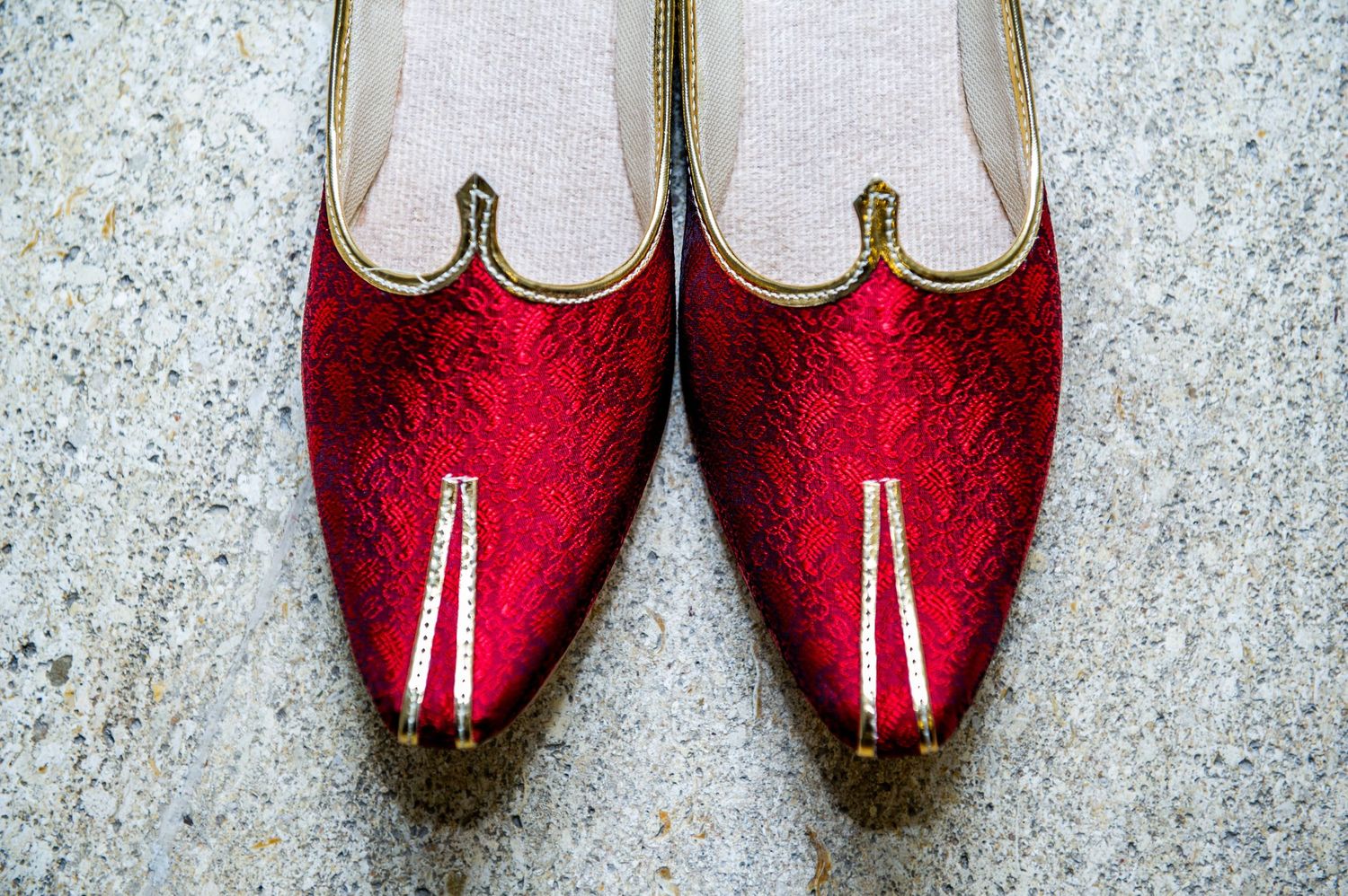 Red embroidered Indian juttis with gold trim and pointed toes displayed on a marble surface.