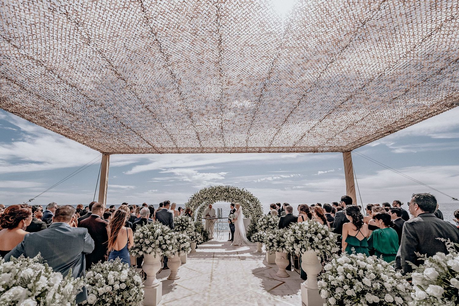 Outdoor wedding ceremony setup with white floral arrangements and draped fabric canopy.