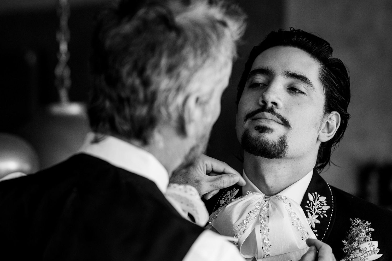 Black and white photo of a father adjusting his sons boutonniere before a wedding ceremony.