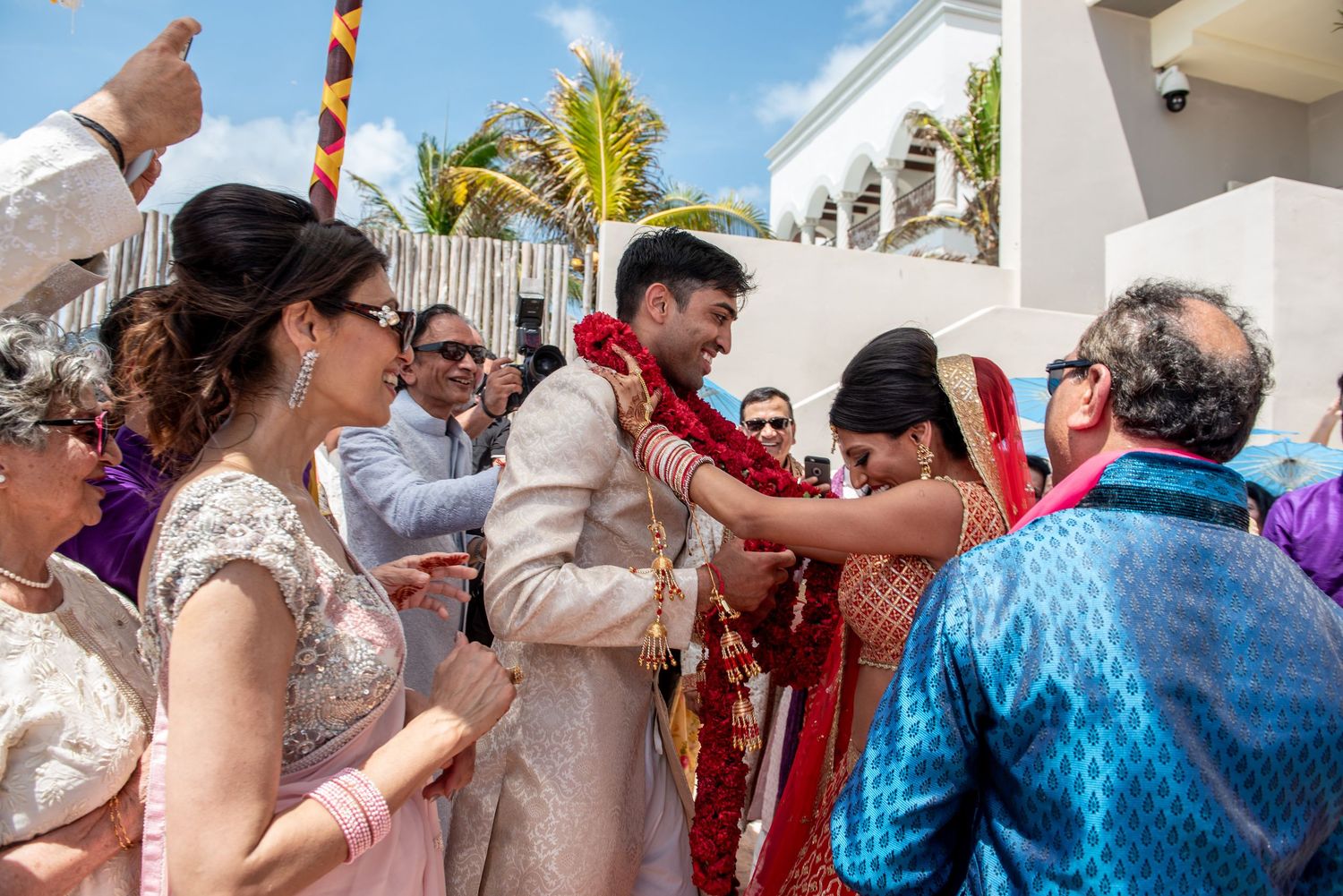 Guests celebrate with bride and groom during a vibrant outdoor Indian wedding ceremony in a tropical setting.