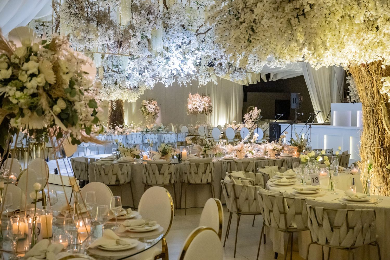Wedding reception space illuminated with warm lighting featuring elegant table settings and floral arrangements.