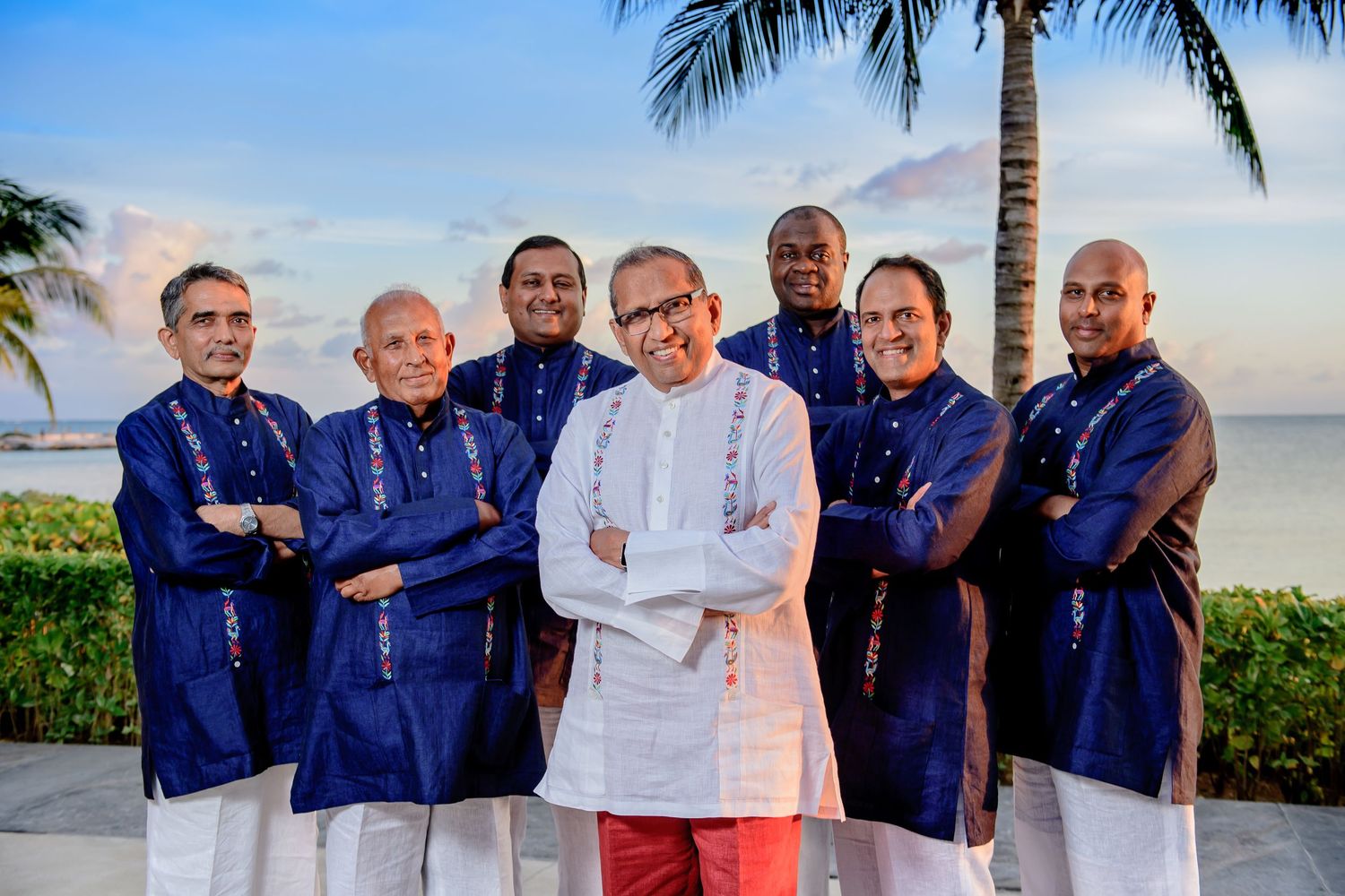 Groomsmen in navy blue shirts pose together on tropical beach at sunset.