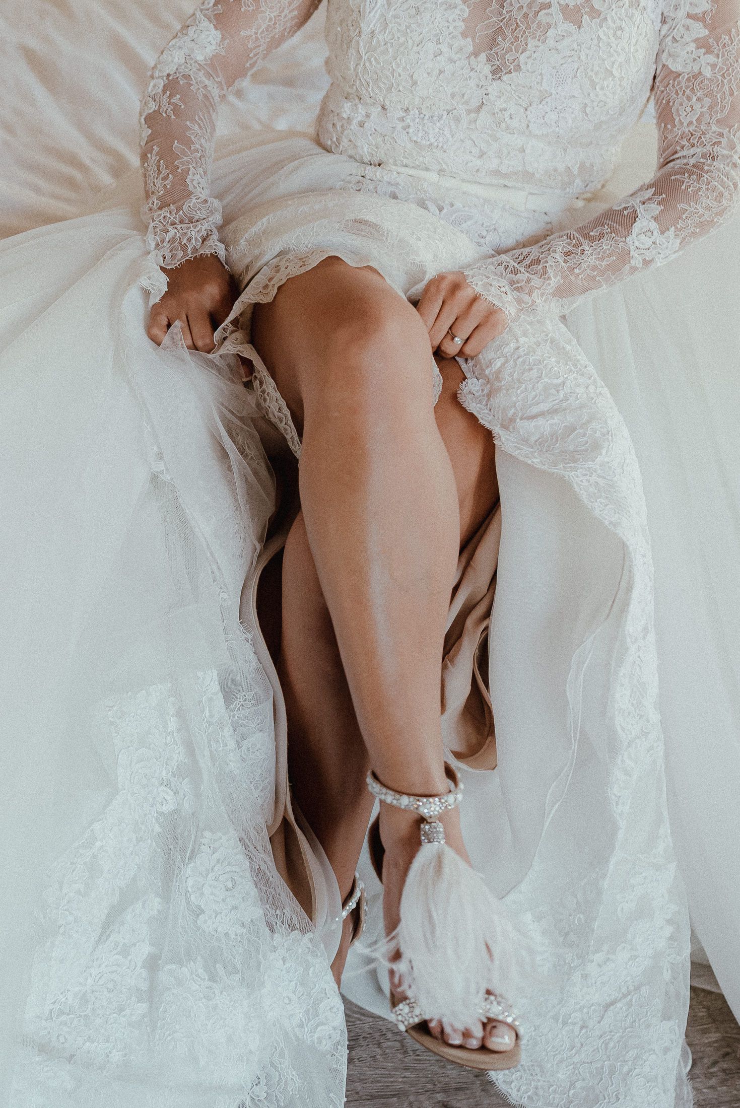 Close-up detail of a white lace wedding dress and legs against a light background.