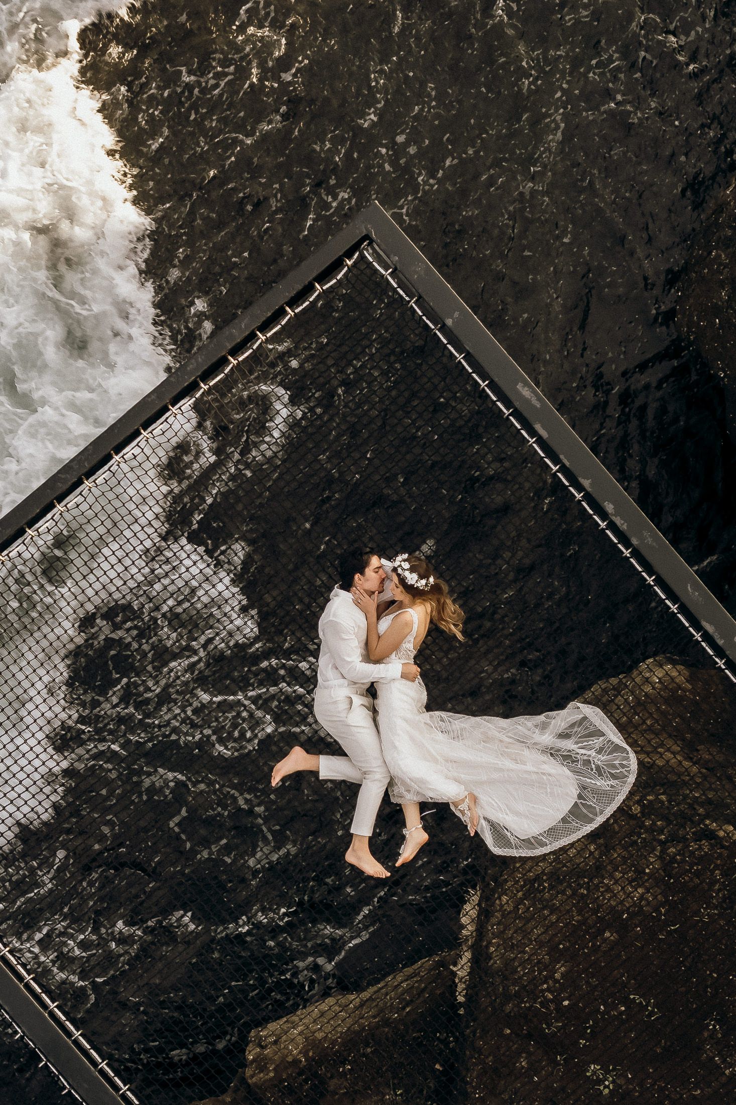 Aerial view of couple in white lying on dark textured surface creating artistic contrast.