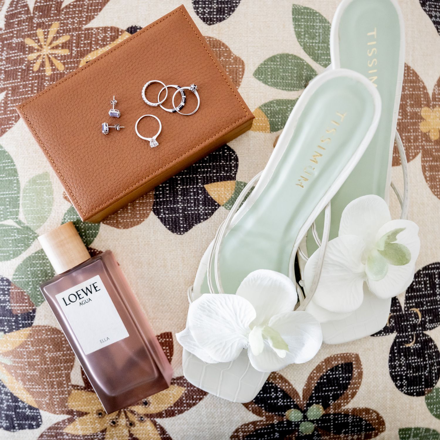 Wedding accessories including rings and perfume arranged with white flowers.