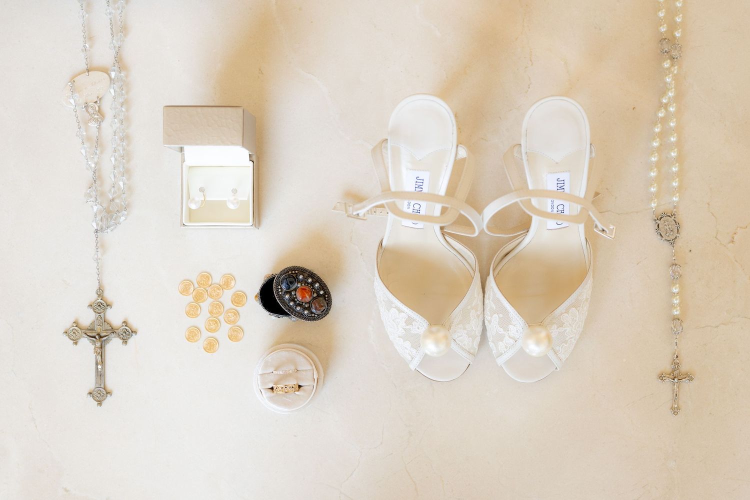 Wedding accessories including crystal shoes and religious symbols arranged on light background.