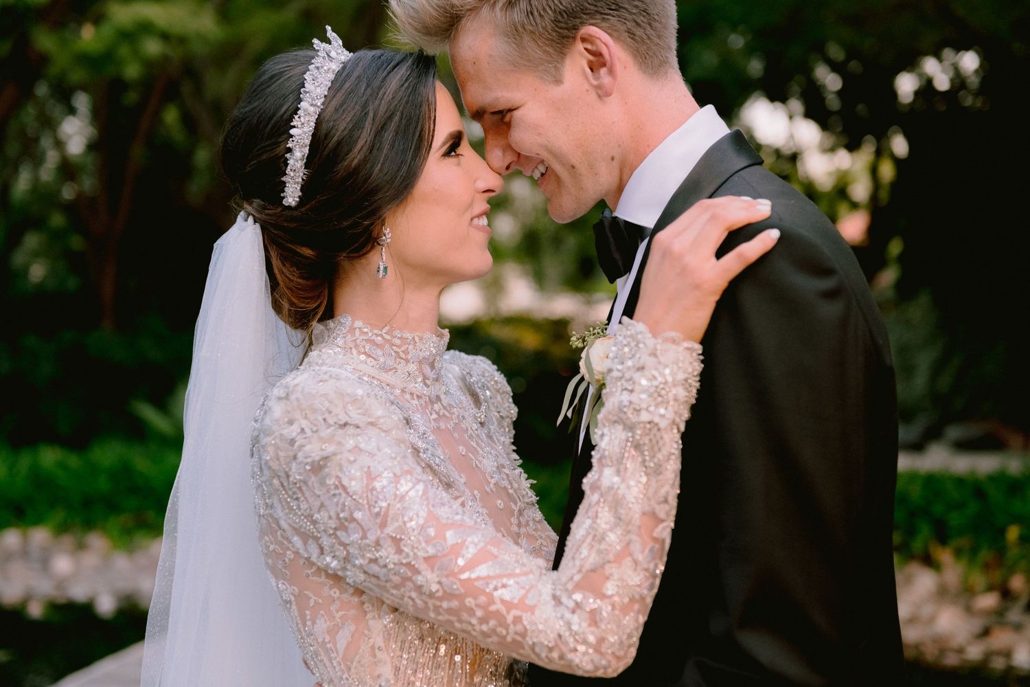A bride and groom share a romantic moment outdoors, with the bride wearing a beaded gown and veil.