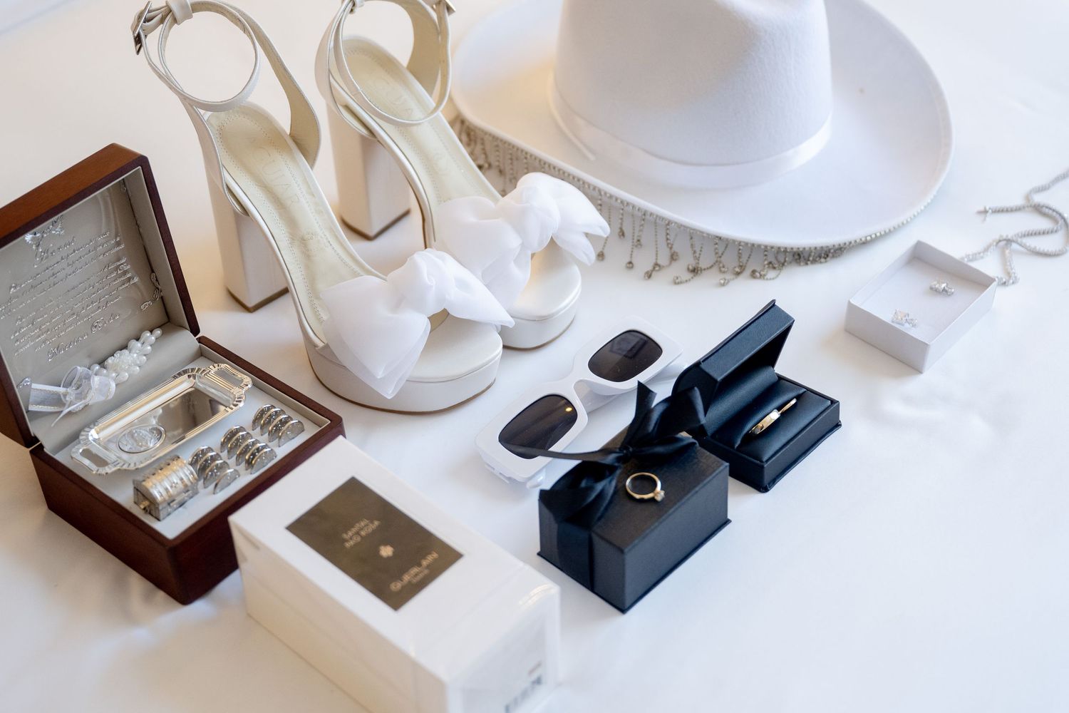 Wedding accessories including white shoes, jewelry boxes, and decorative items arranged on white surface.