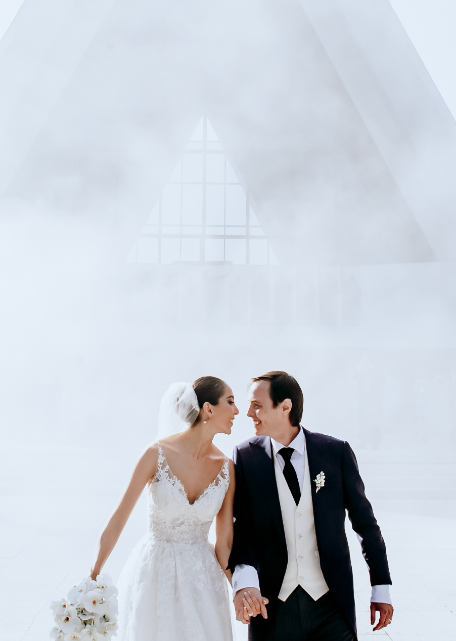 Modern minimalist wedding photo of couple against white architectural backdrop.