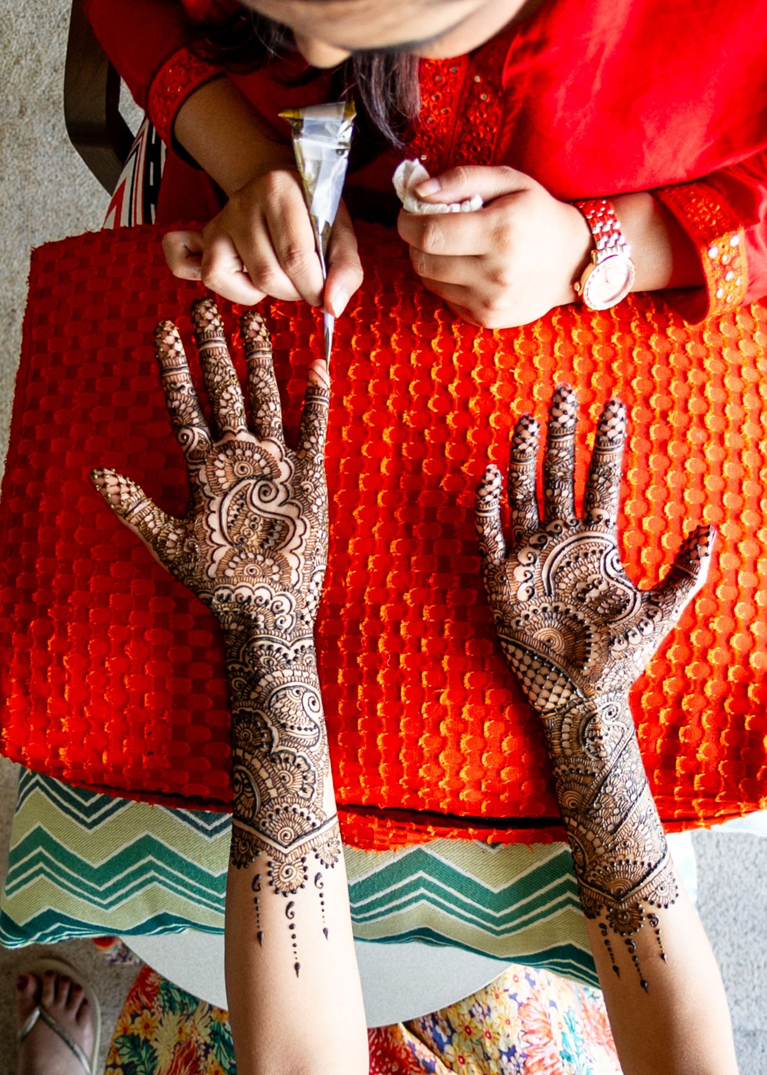 Intricate bridal mehndi henna designs on both hands, with detailed paisley patterns, against a red background.