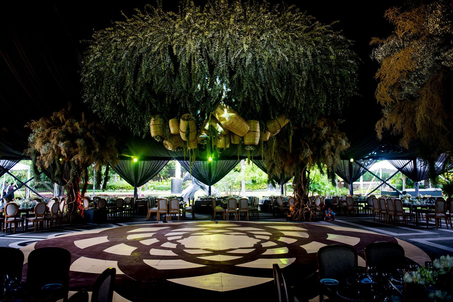 Elegant outdoor event venue at night with lush trees, decorative lights, and patterned dance floor.