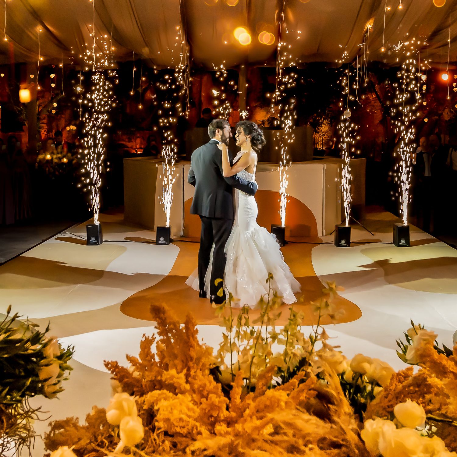 Wedding reception dance floor surrounded by sparklers and golden floral decorations.