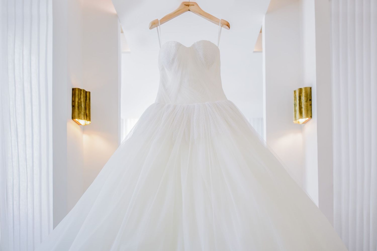 White wedding dress hanging in an elegant room with modern gold light fixtures.