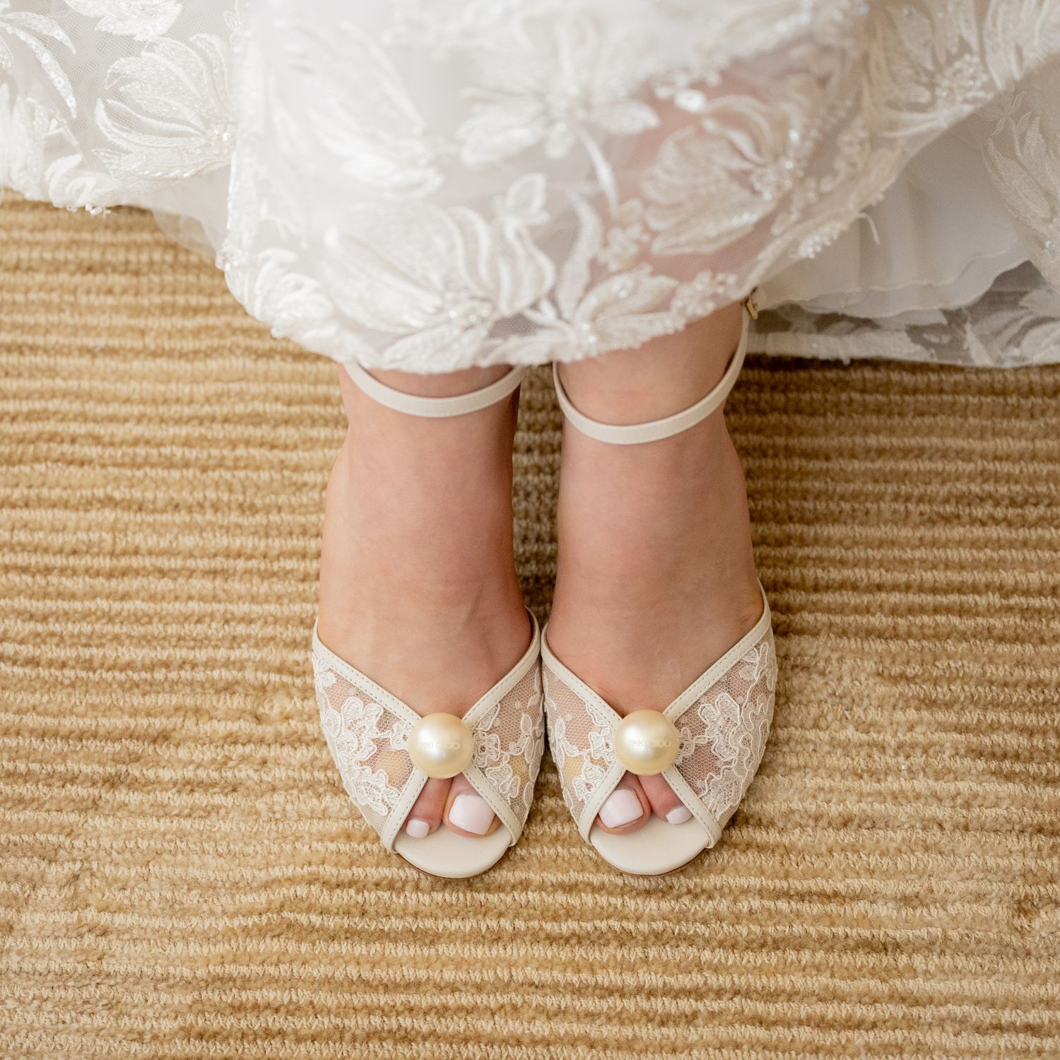 Elegant white bridal shoes with lace details on a beige carpet.