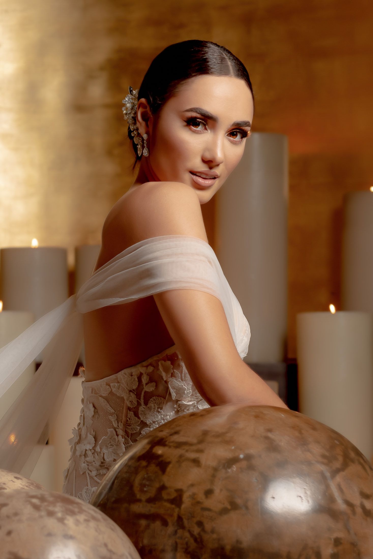 Bride wearing a detailed lace wedding dress poses against a warm-toned background.