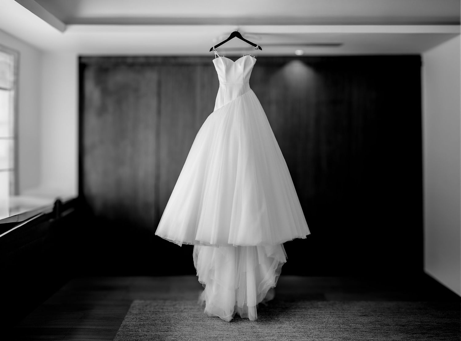 Elegant strapless ball gown wedding dress hanging on a hanger in black and white photography.