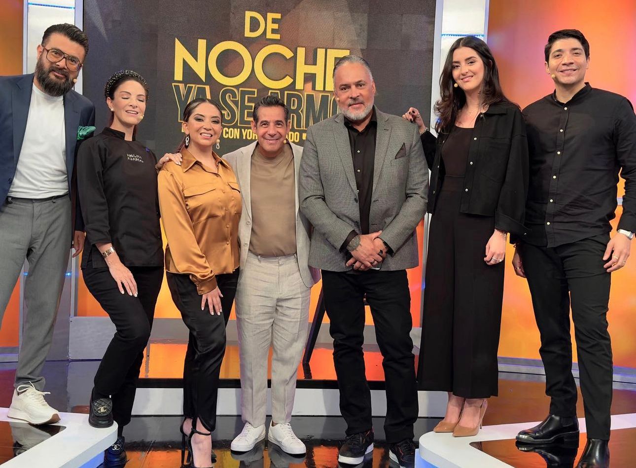 Group photo on television set with show title and orange-toned studio lighting.