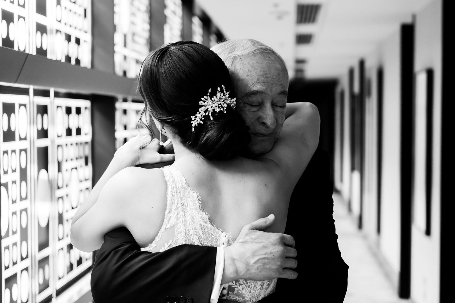 Black and white photo of people embracing in an emotional moment at what appears to be an airport or station.
