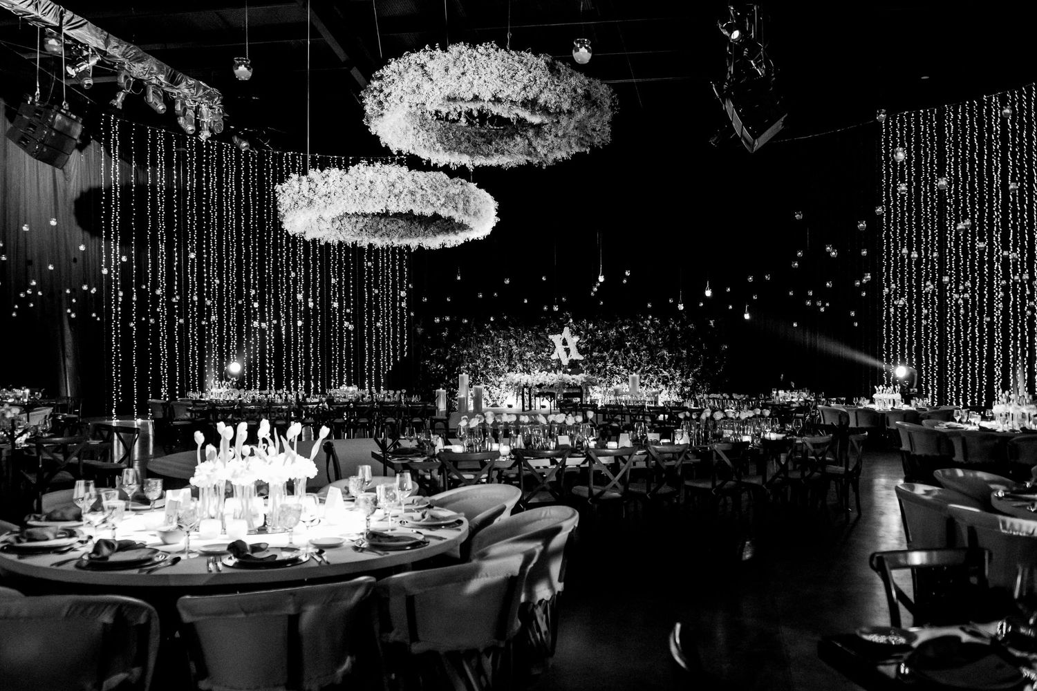 Elegant black and white gala event with chandelier lighting, round dining tables, and sparkling decor.