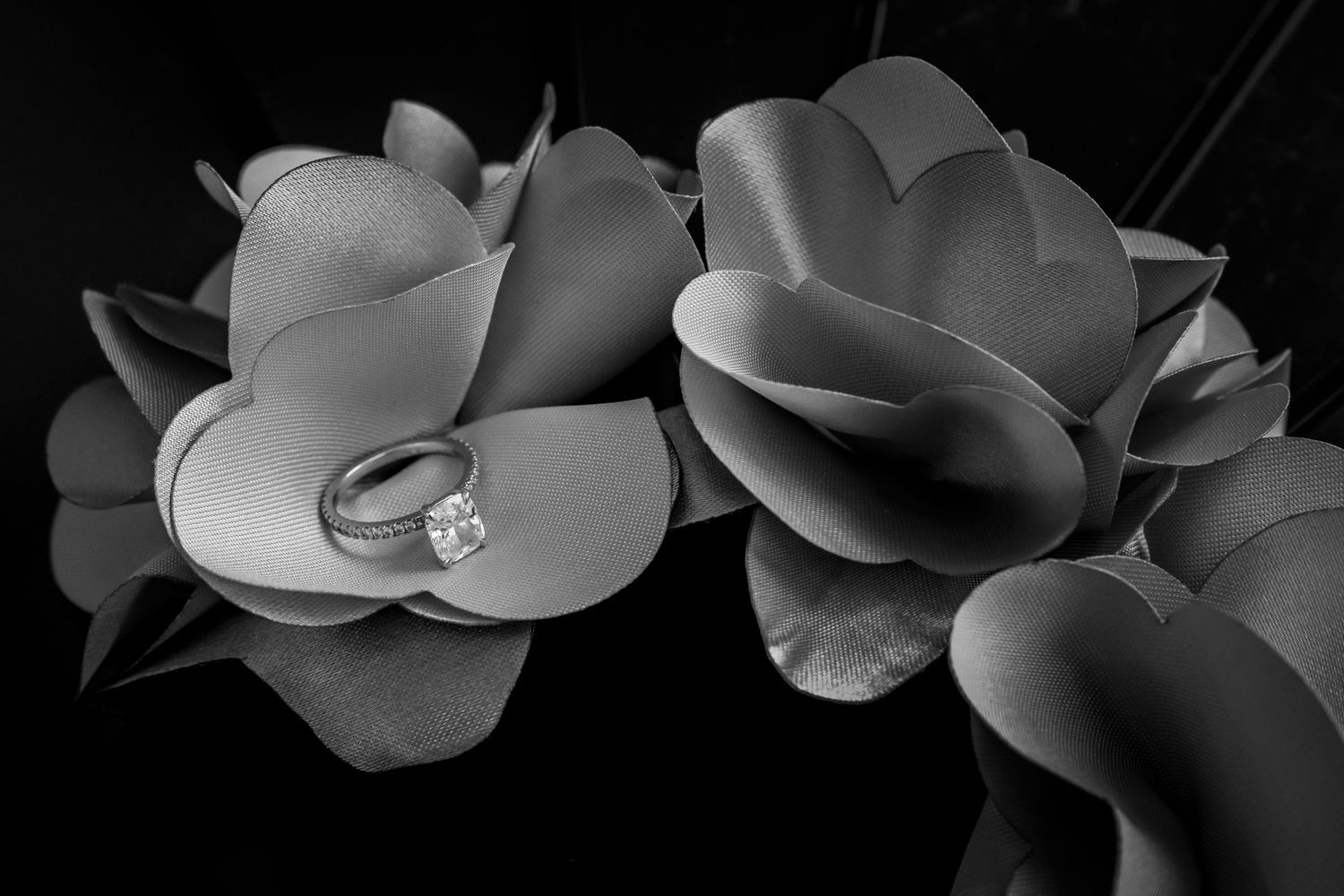 Black and white photo of a diamond engagement ring resting on artificial roses.