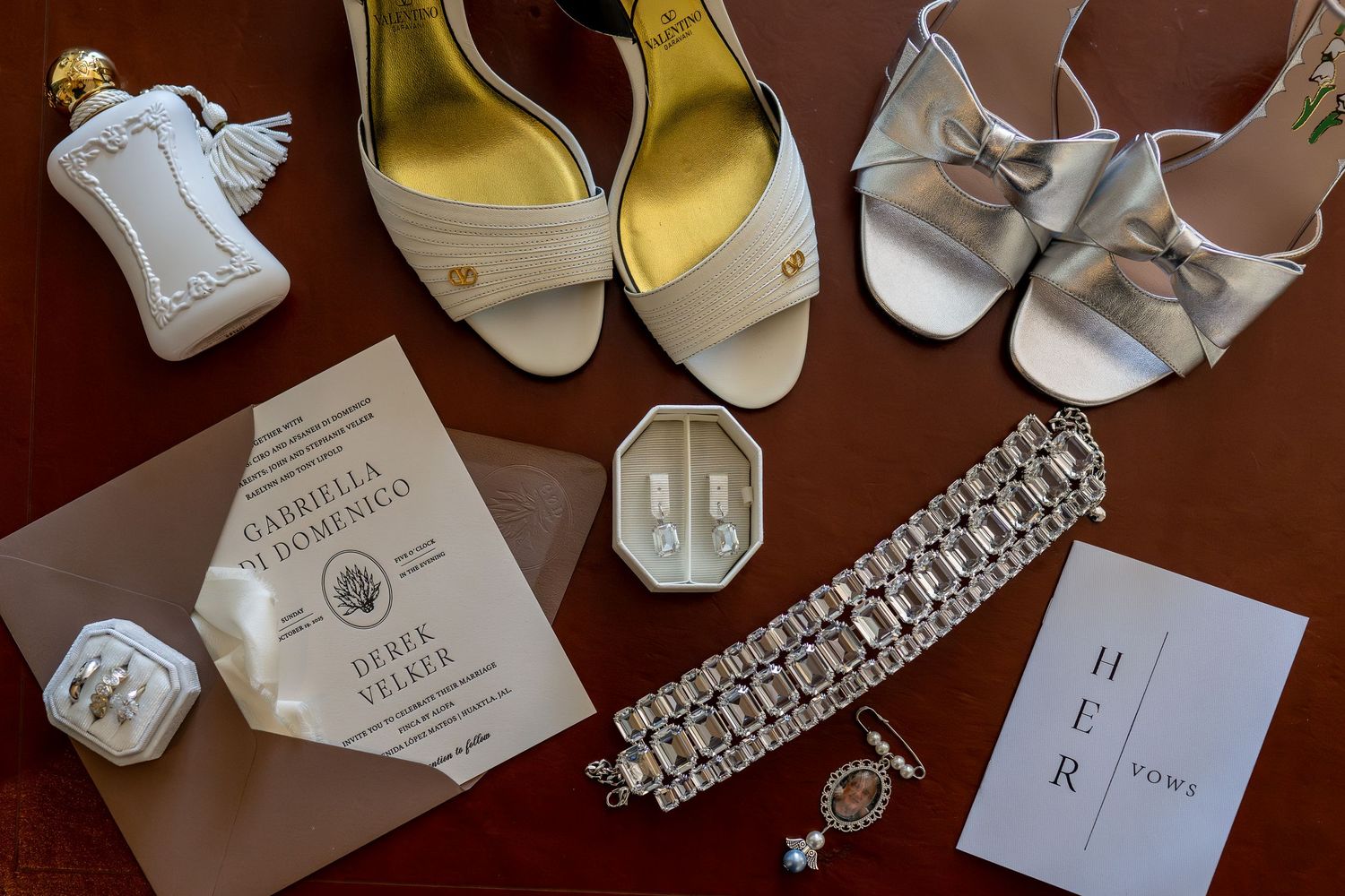 Wedding details including shoes, jewelry and invitation cards on dark wooden surface.