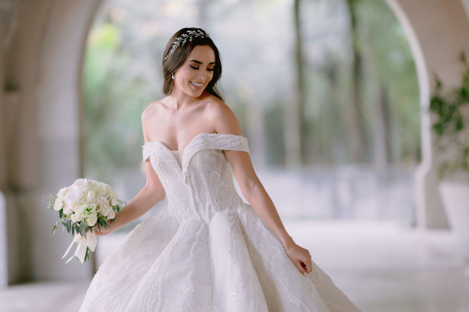 Dreamy bridal portrait with flowing ball gown and off-shoulder neckline in natural setting.