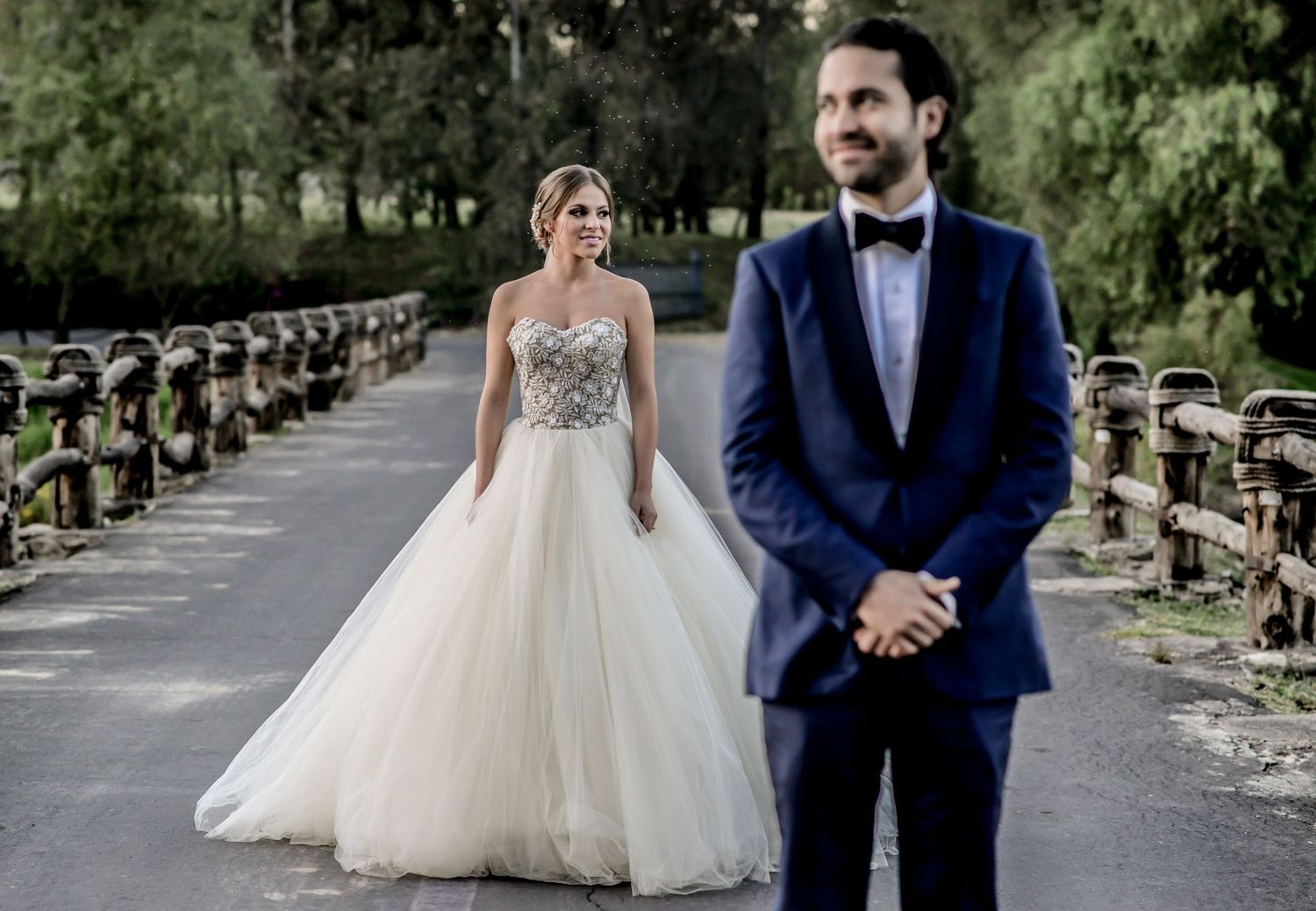 Wedding couple walking through a tree-lined path in formal attire.