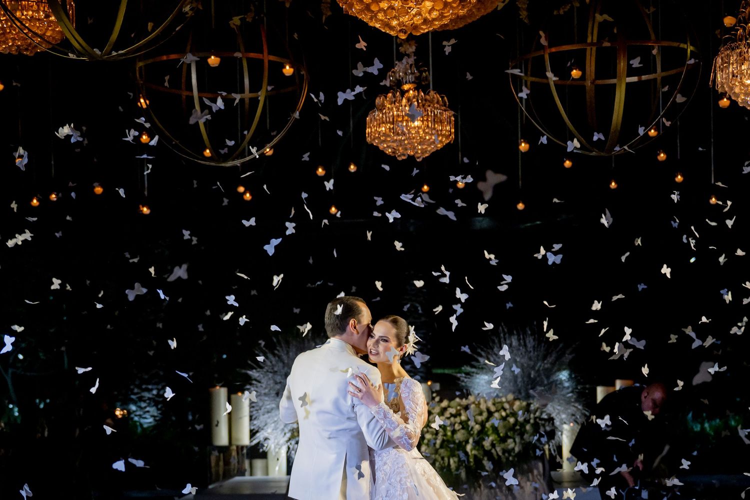 A romantic wedding dance under crystal chandeliers with floating confetti creates an enchanting scene.