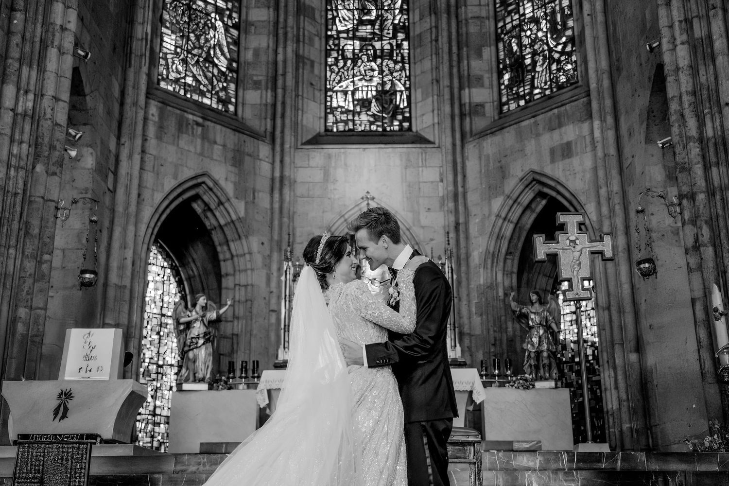 Black and white photo of a bride and groom sharing a romantic moment at the altar of a Gothic church.