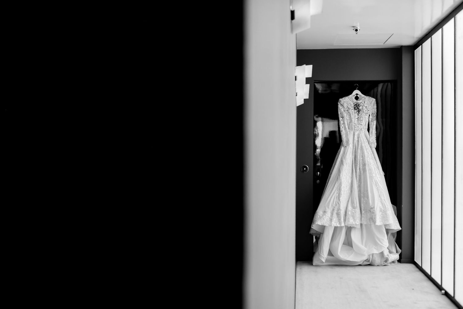 Stunning white wedding dress hanging in a doorway, captured in classic black and white photography.