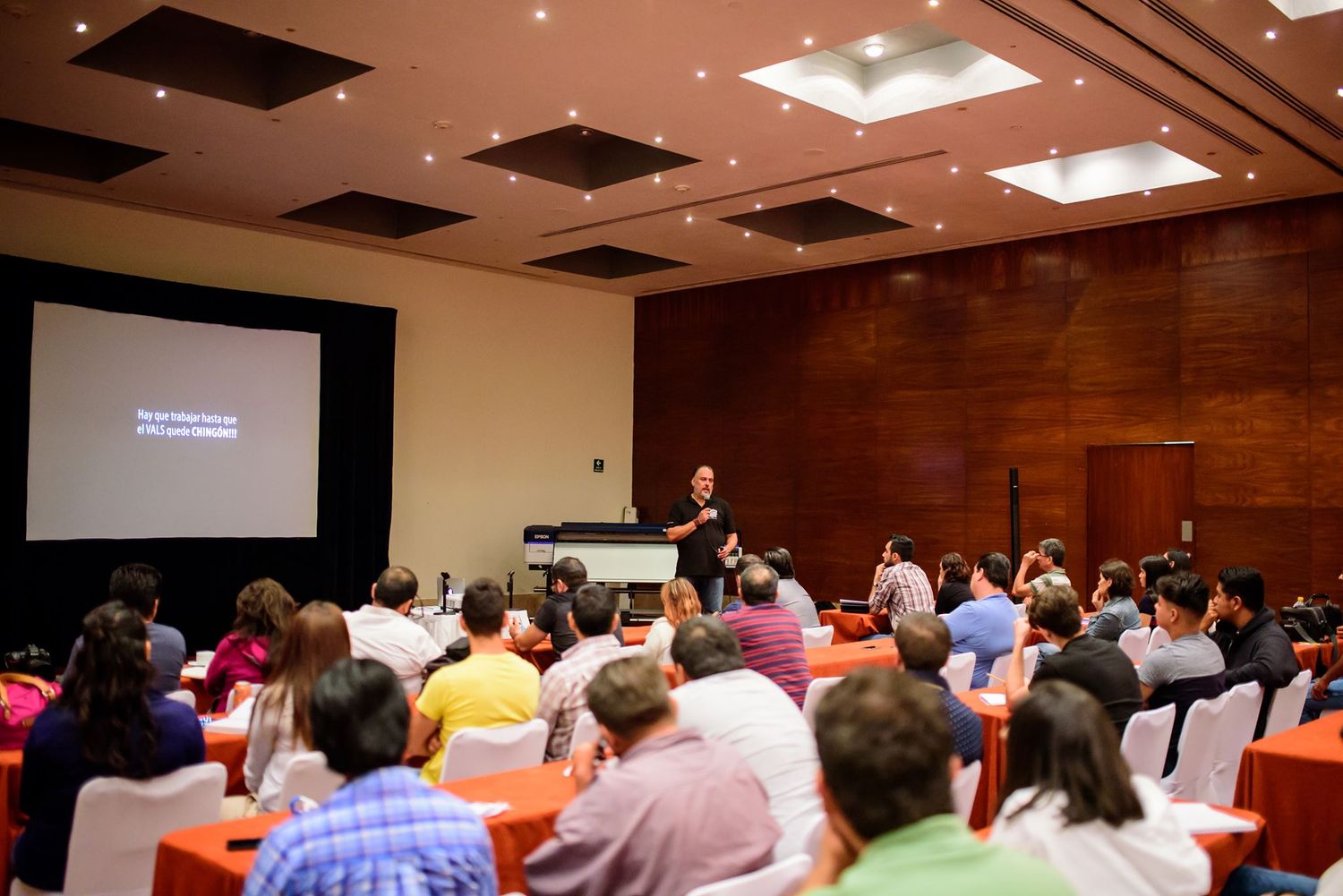 Wide shot of a crowded conference room with attendees seated at tables during a presentation.