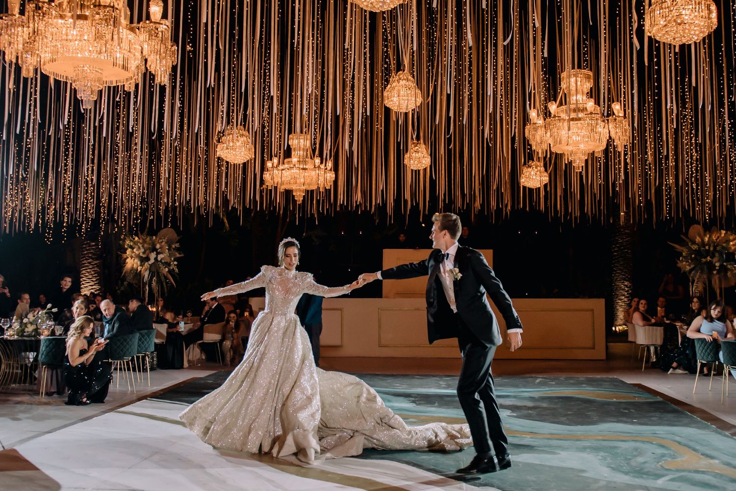 Bride and groom share first dance under crystal chandeliers and golden hanging decor at elegant wedding reception.