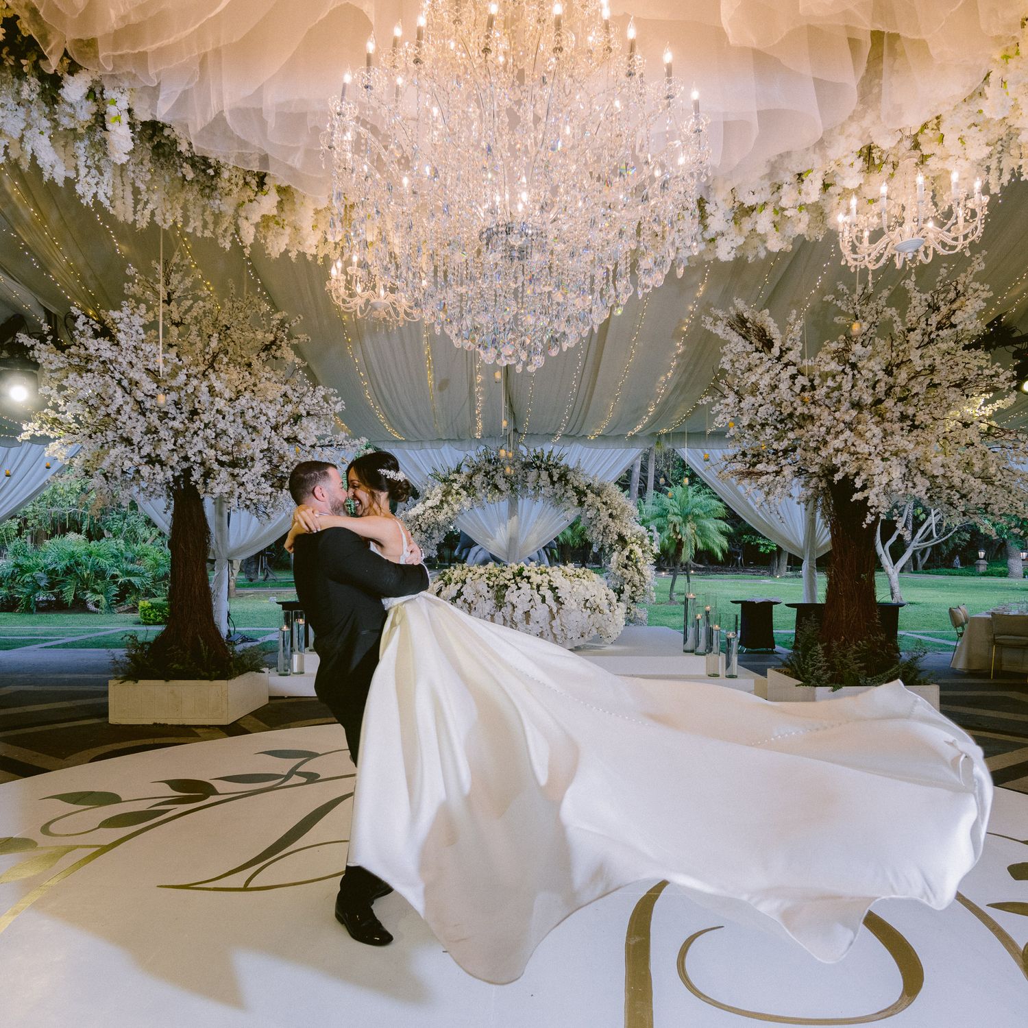 An elegant wedding dance under crystal chandeliers and white floral decorations.