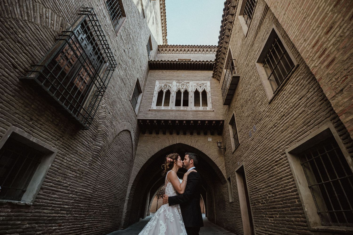 Wedding couple embracing under historic brick archway.
