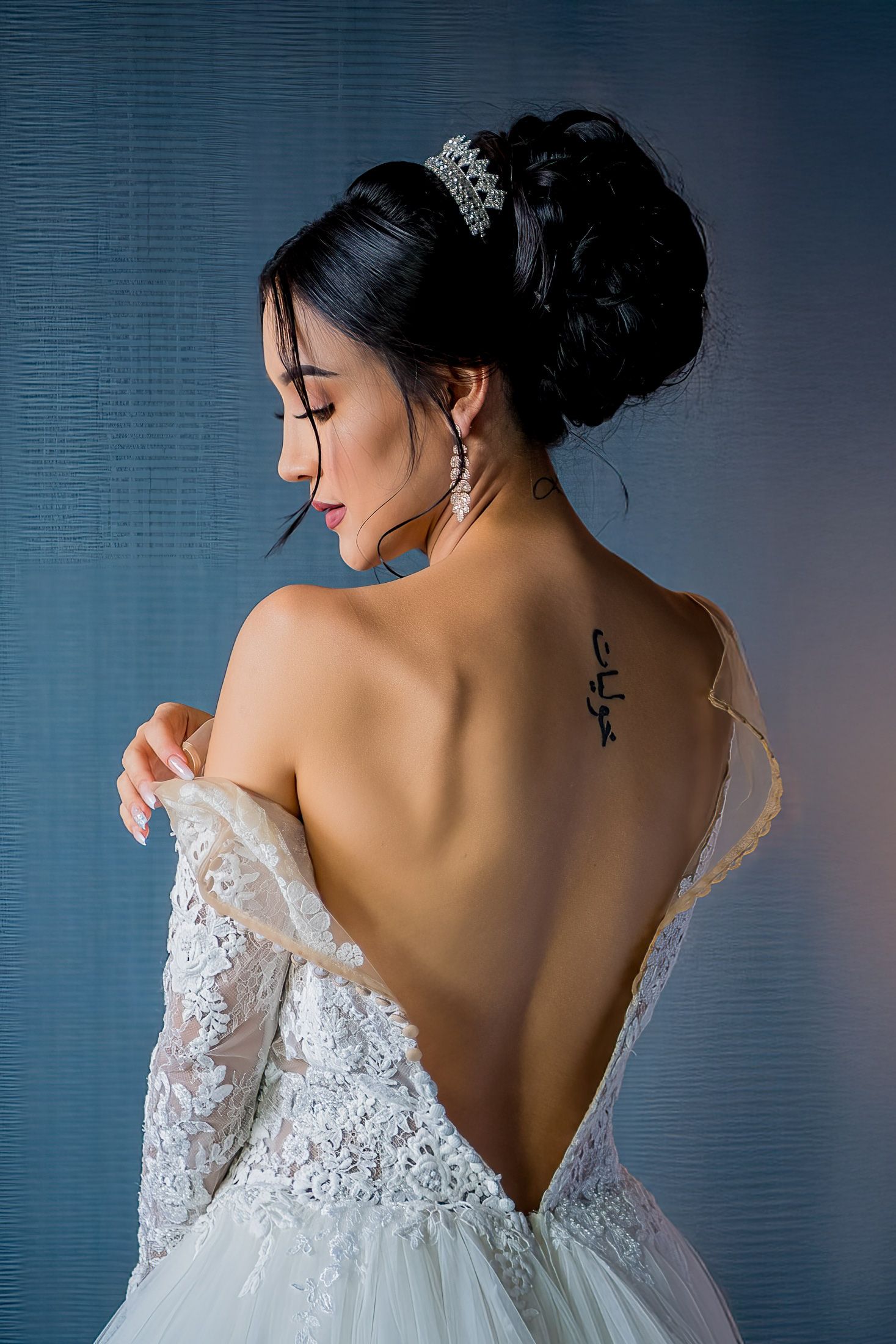 Elegant backless wedding dress with lace details against blue background.