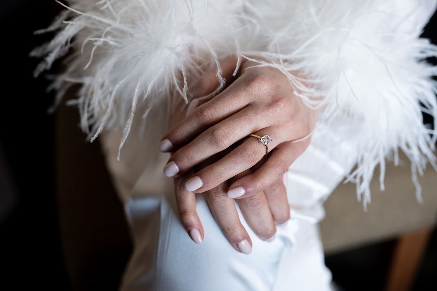 Detail of feathered white bridal accessory with diamond ring.