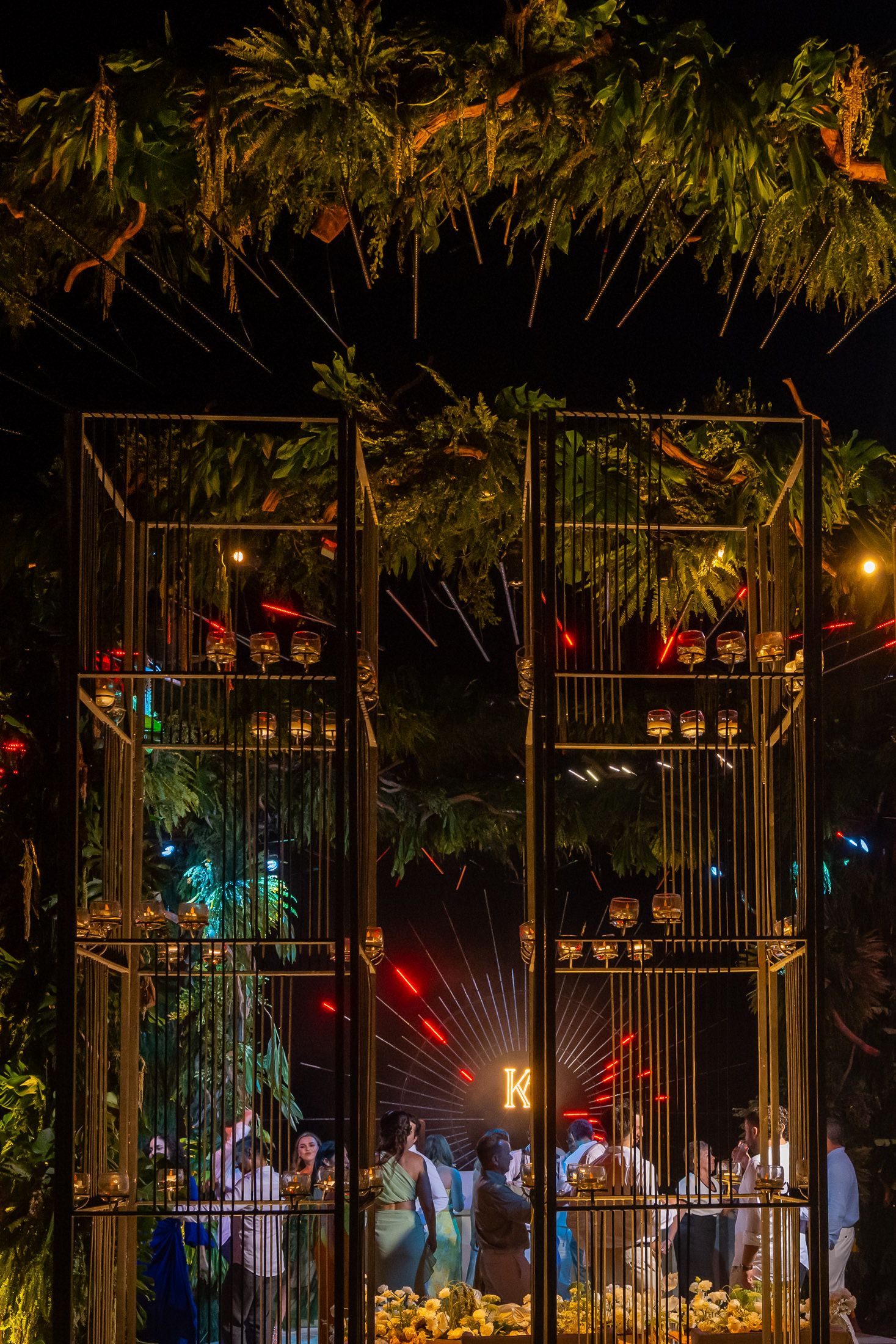 Illuminated garden gates with hanging lanterns and decorative lights create a magical nighttime entrance.
