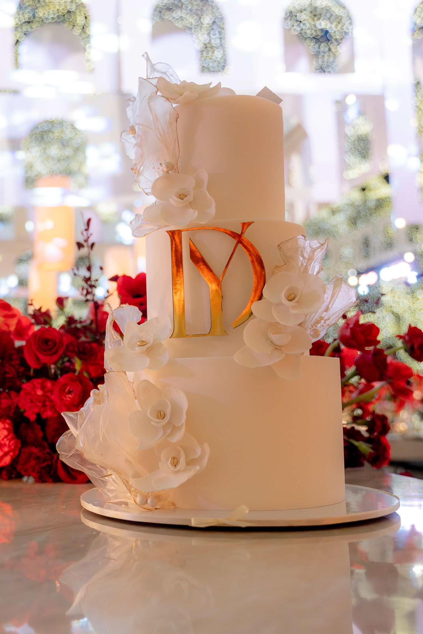 Elegant white wedding cake adorned with sugar flowers and red floral accents.